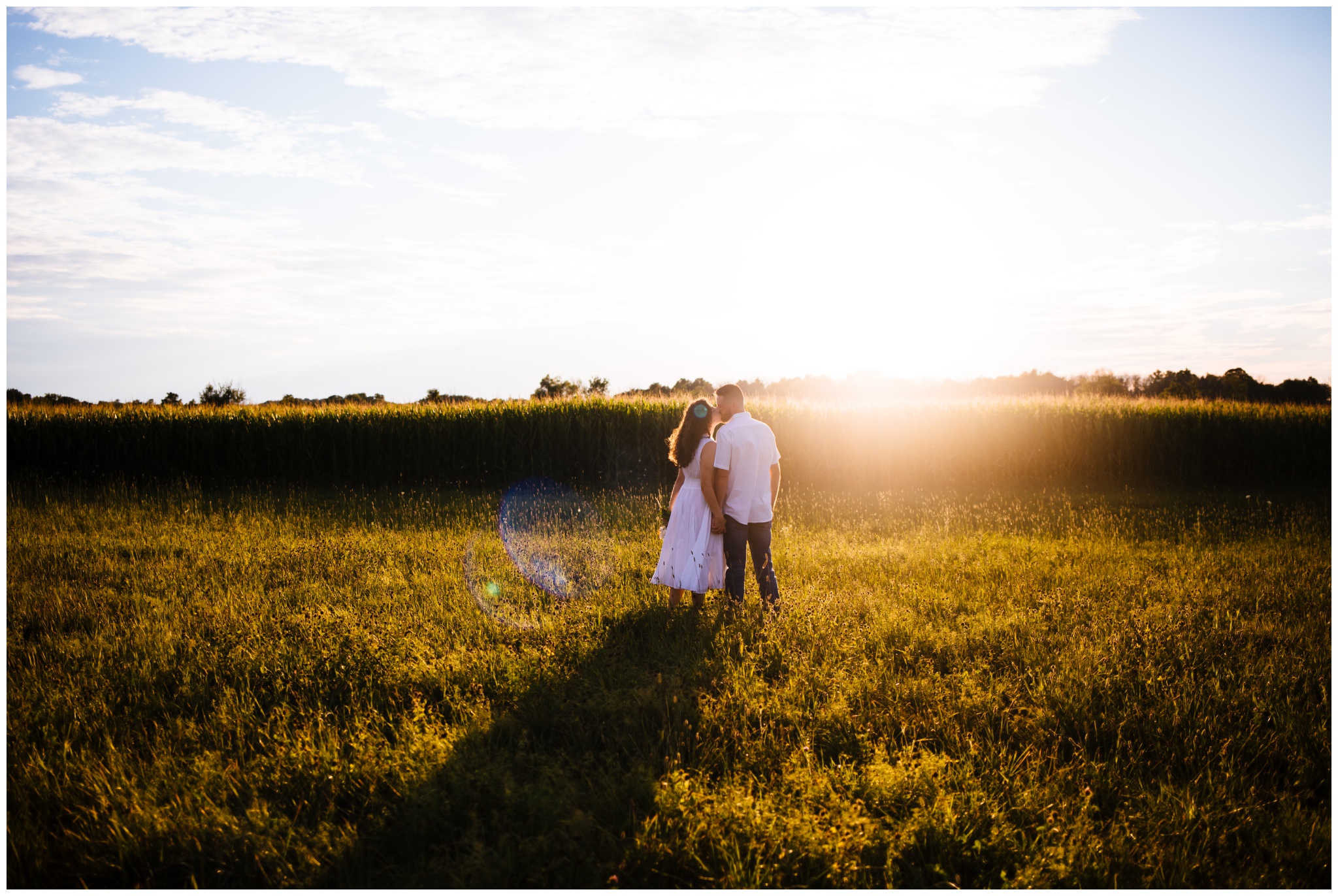 A woman and a man stand in a field during golden hour and kiss during their Syracuse engagement session.