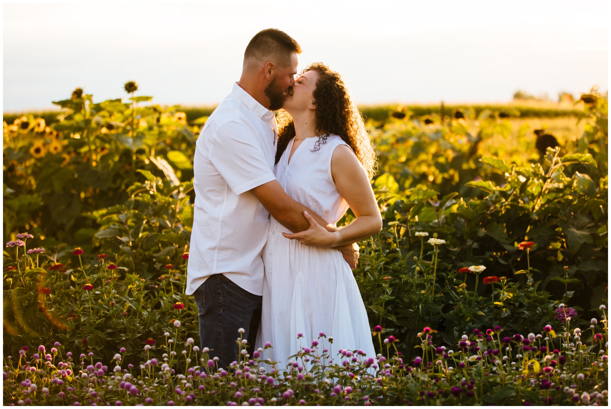 A couple kisses in a field of wildflowers during their summer engagement session on a farm.