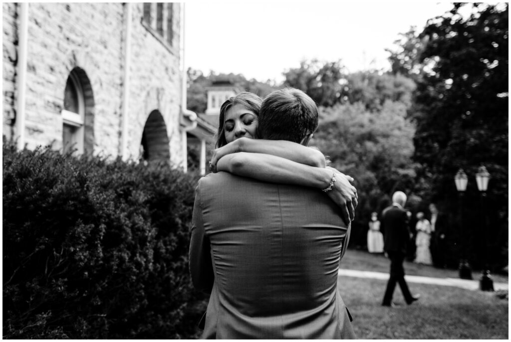 A black and white photo of the bride hugging the groom. A single tear falls down her face, during an emotional first look at their Ithaca Farmer's Market Wedding.