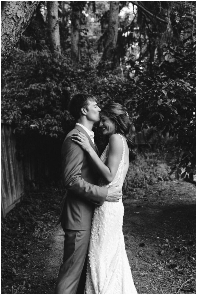 a black and white portrait of the bride and groom on their wedding day. The groom kisses the bride on the forehead while the bride smiles. They did wedding portraits at Fountain Place Ithaca.