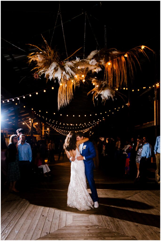 The bride and groom share their first dance under twinkle lights and a stunning feather and floral arrangement at the Ithaca Farmer's Market.