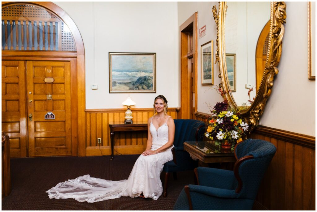 a bride sits on a chair posing in her wedding gown upstairs at belhurst castle.