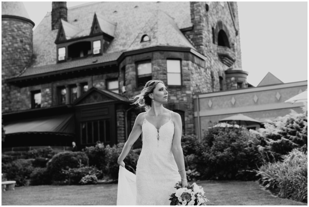 a bride holds on to the tail of her dress with belhurst castle in the background.