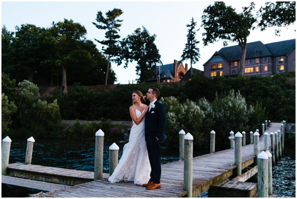 bride and groom stand on the dock with belhurst castle behind them.