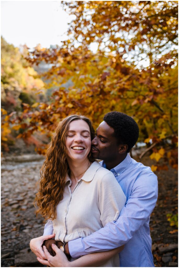 a couple snuggles together with smiles on their faces during their ithaca engagement session.