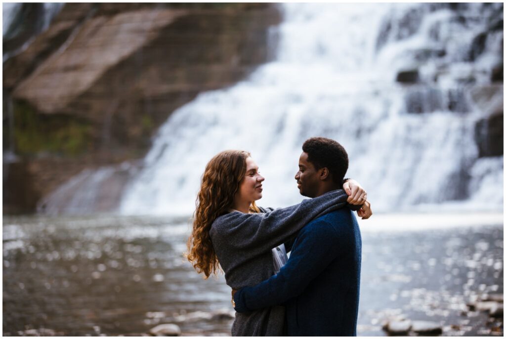 girl wraps her arms around fiances neck at ithaca falls during their engagement session.