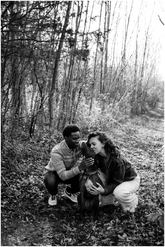 Black and white photo of a couple snuggling their dog during their engagement photos.