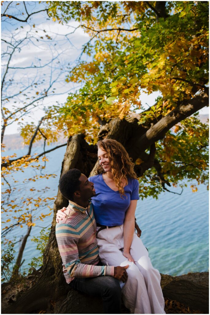 Girl sits on guys lap and they look at each other during their engagement photos.