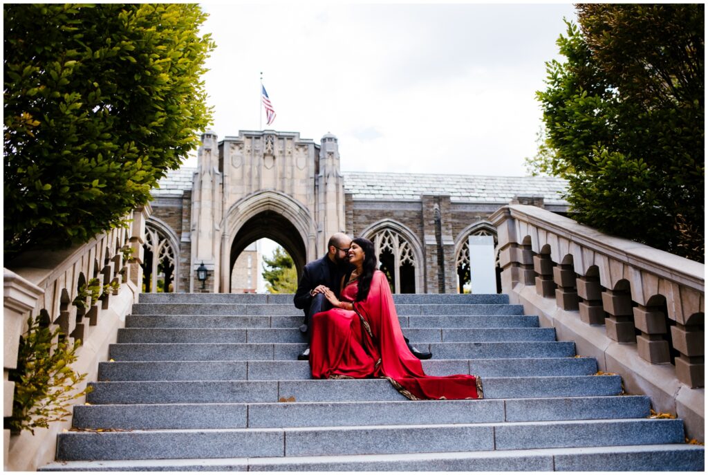 A couple sits on a set of stairs at Cornell University. The woman is in a traditional red sari during their engagement session.