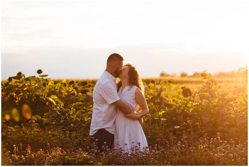 A couple kisses in the middle of a wild flower field at sunset.
