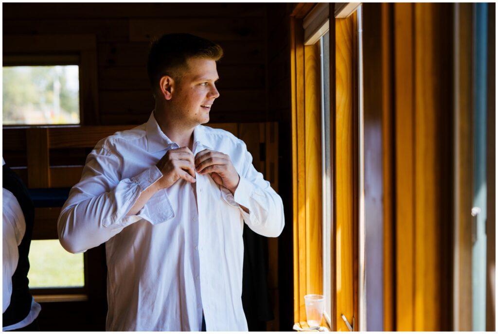 groom gets ready by buttoning his shirt.