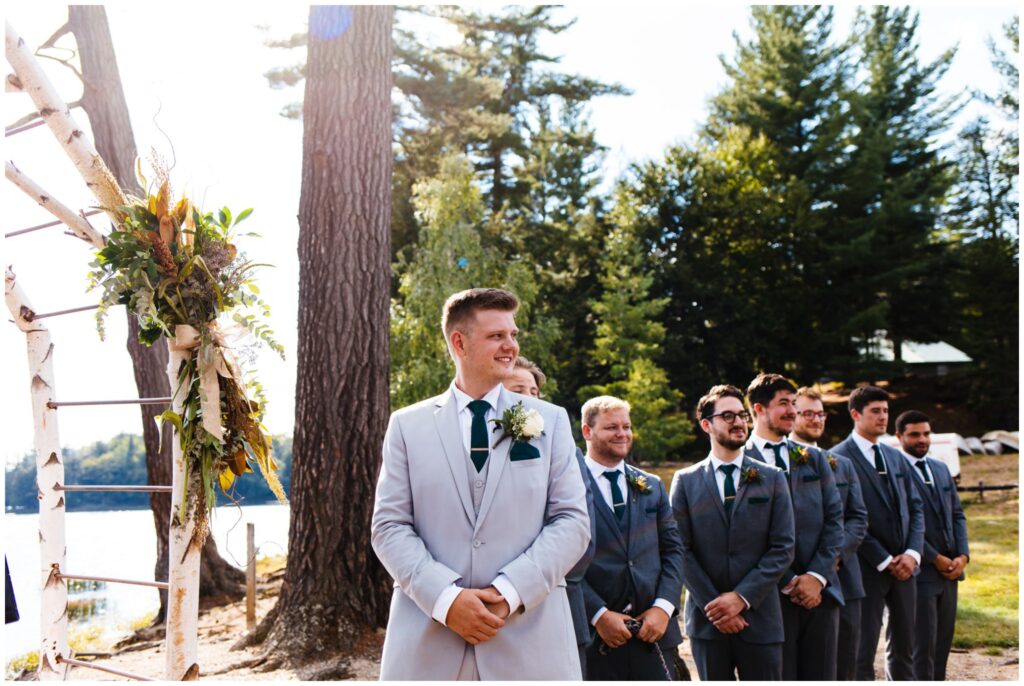 Groom waits at the end of the aisle for the bride during their wedding ceremony.