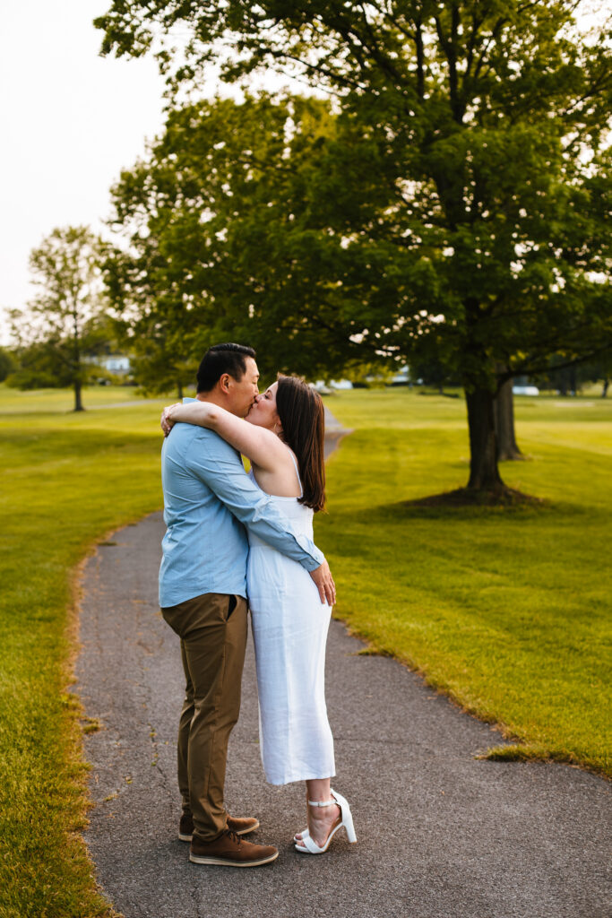 A couple stands on a path and kisses during their golden hour engagement session.