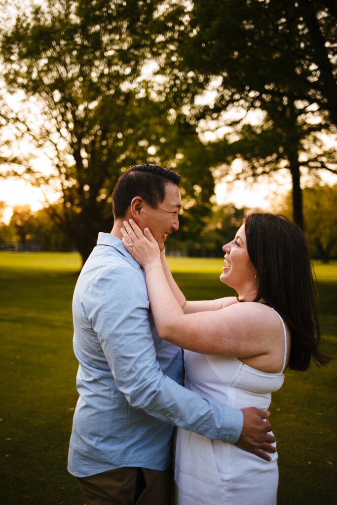 a woman holds her fiance's face as they laugh during their rochester engagement session.