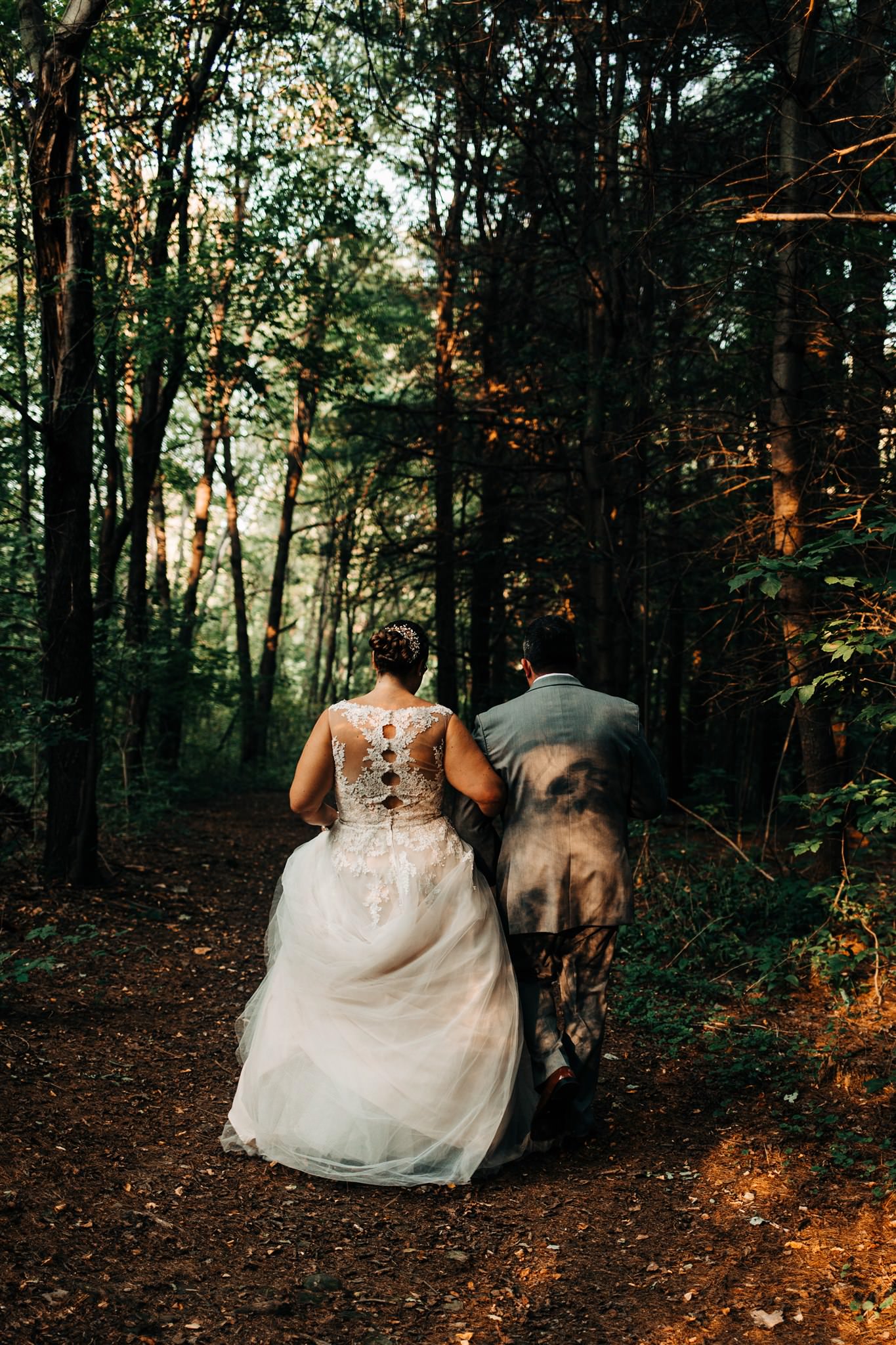 The bride and groom walk through dappled light in the woods on the way back to the fontainebleau Inn.