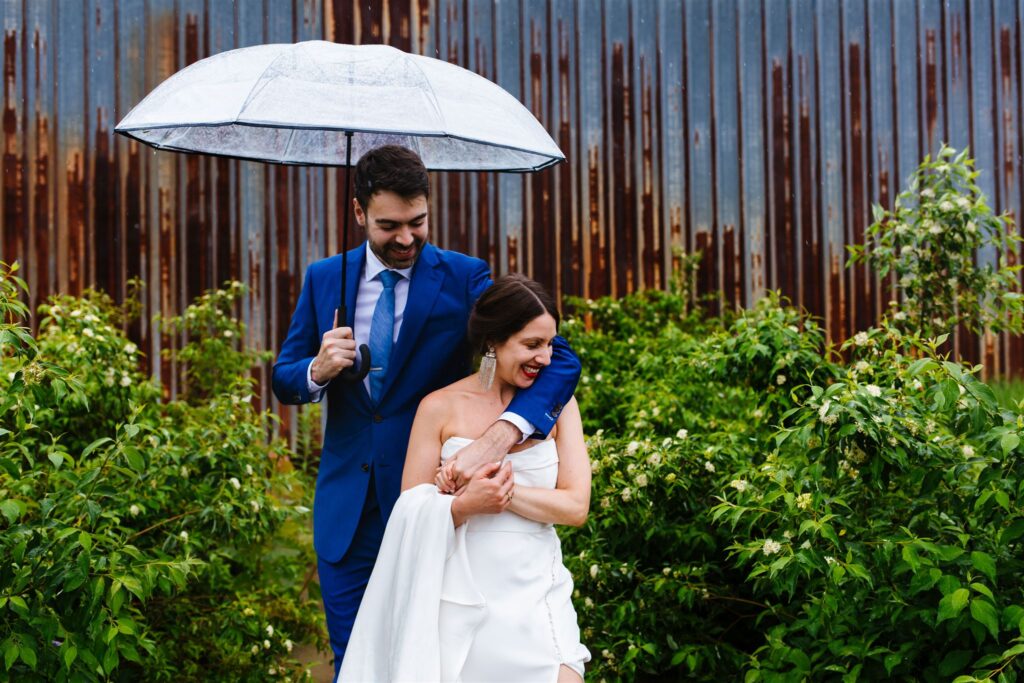 Bride and groom hug under an umbrella on their rainy wedding day in the berkshires at Greylock Works wedding.