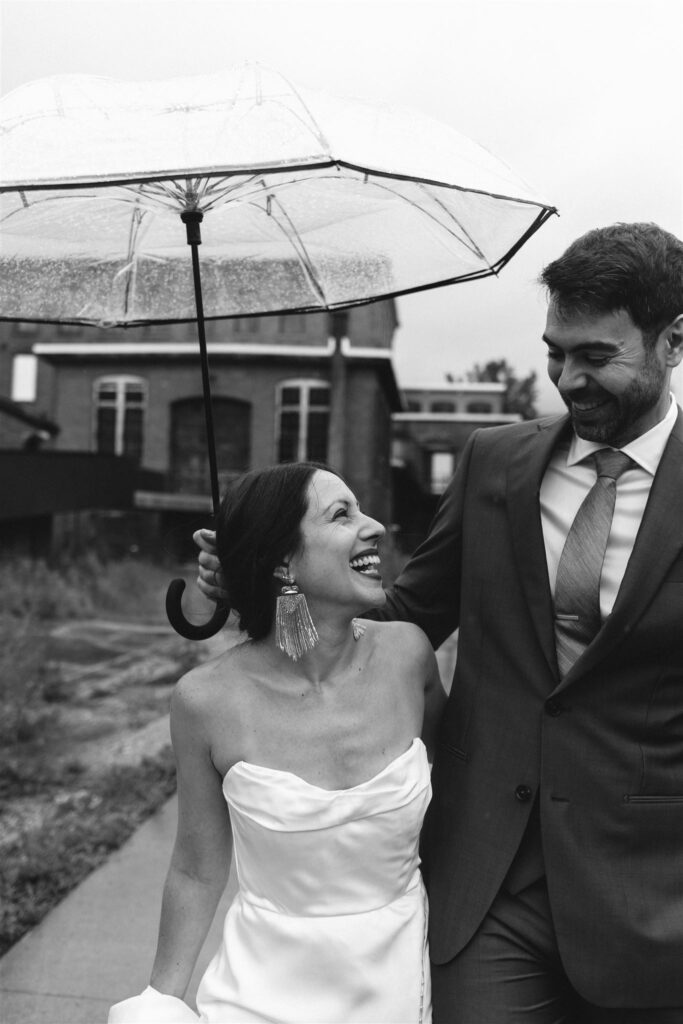 Bride and groom smile at each other under an umbrella at their rainy Berkshire wedding.