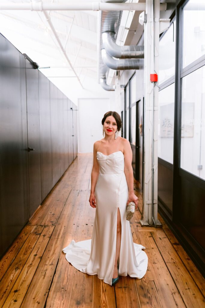 Bride stands in the hallway during her Greylock Works wedding and smiles towards the camera.