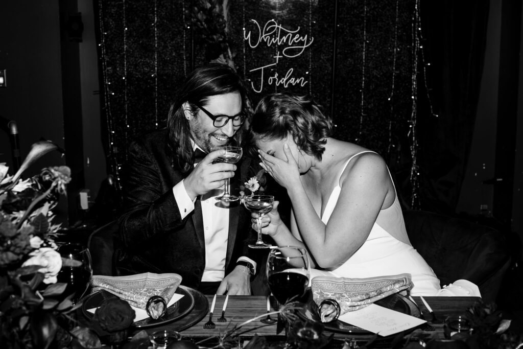 Black and white candid photo of a bride and groom toasting during their wedding at the Gilded club in syracuse, ny. Direct flash wedding photo.