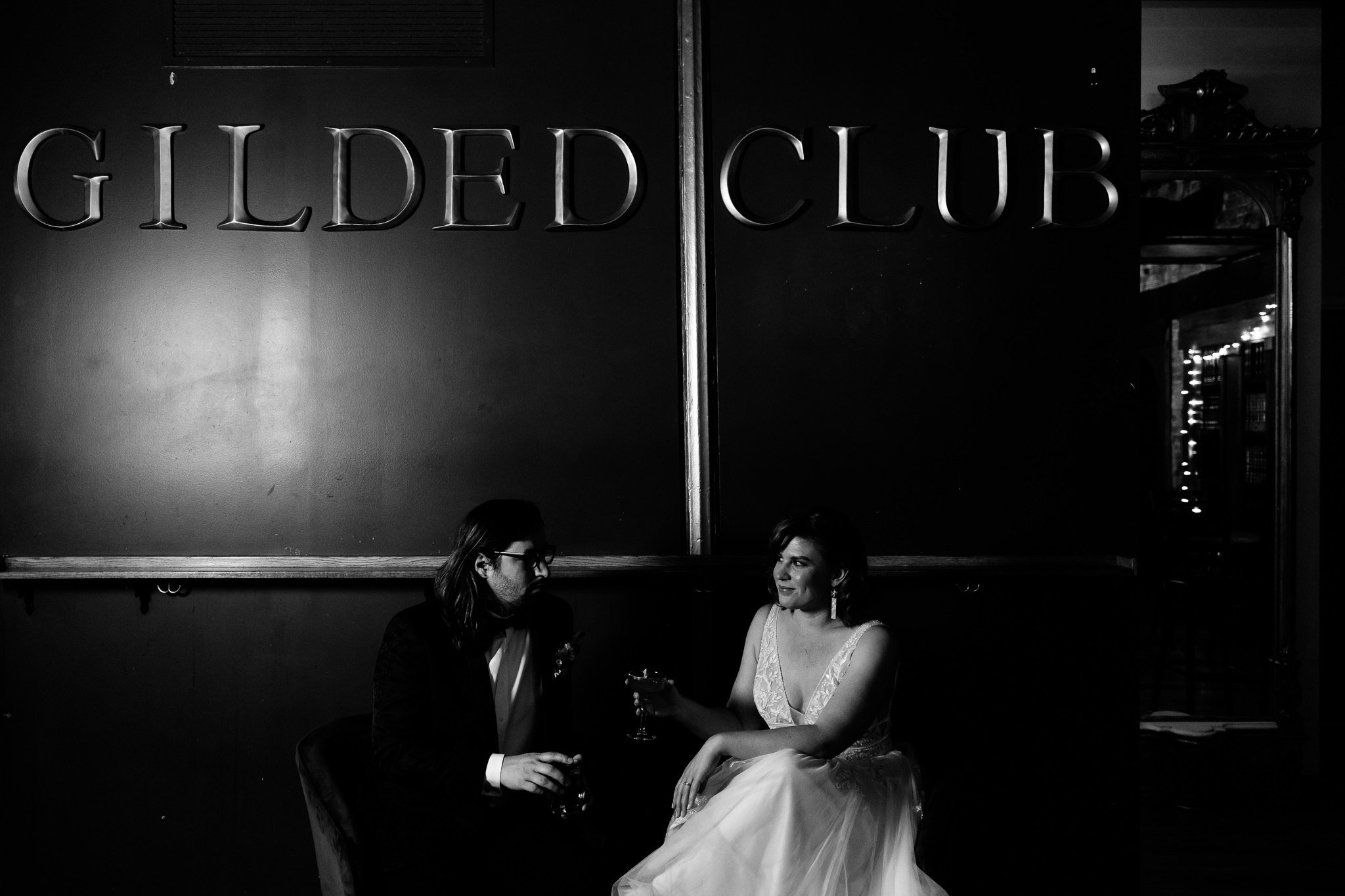 Minimally lit photo of the bride and groom under a sign that says Gilded Club