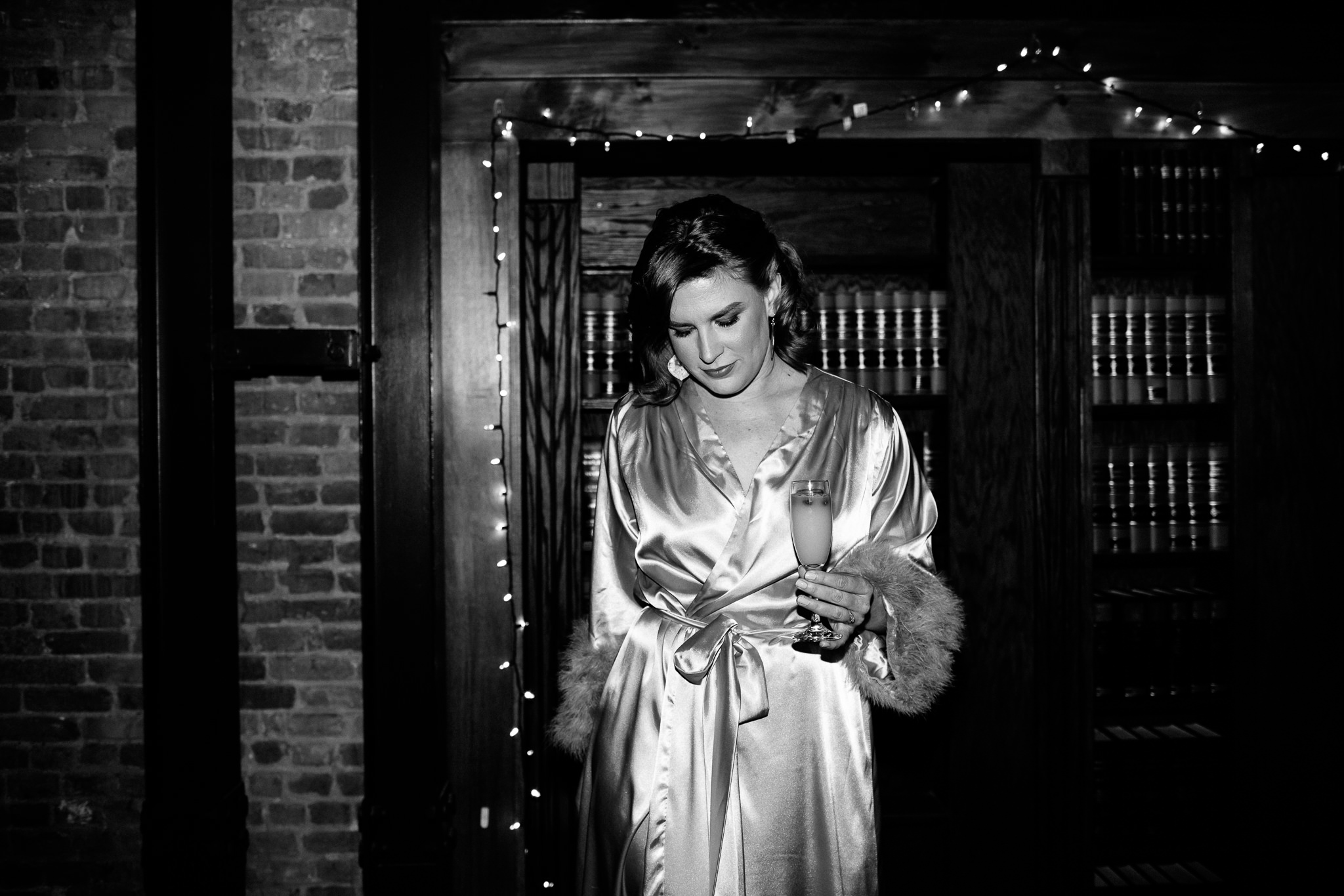 Black and white photo of bride in a robe holding a mimosa. A candid wedding photo at the Syracuse Gilded Club.