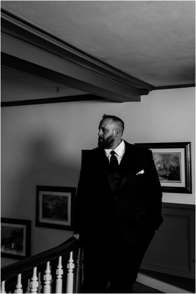 Black and white image of a groom looking out over a stair railing.