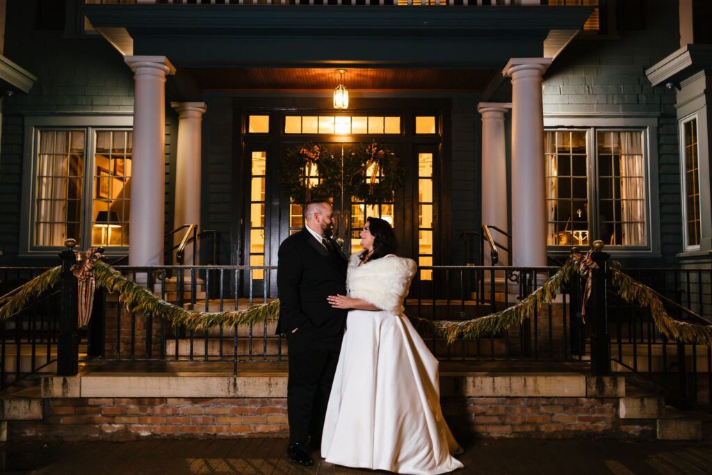 A bride and groom stand in front of the Sherwood Inn at night. 