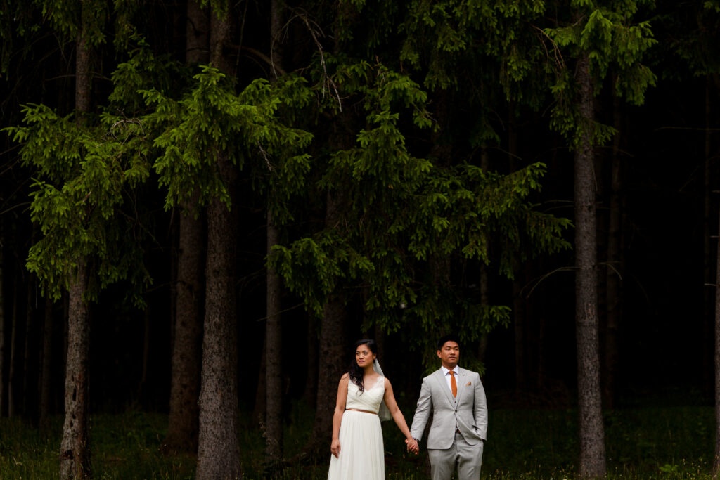 Bride and groom stand among the trees.