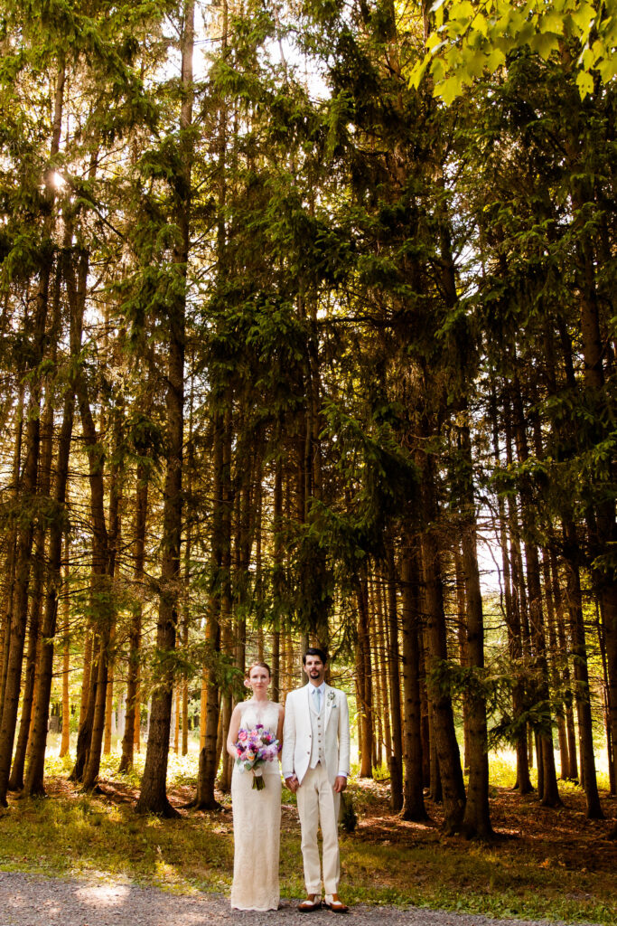 Bride and groom stand in front of pines on their wedding day in Ithaca, NY.