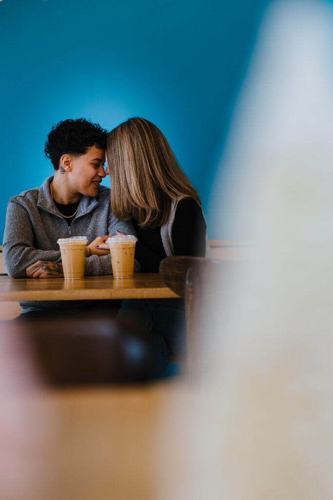 Bride and bride rest their forheads together. photographed by Syracuse wedding photographer Calypso Rae Photography. The couple sits with their coffee inside Sweet Praxis.