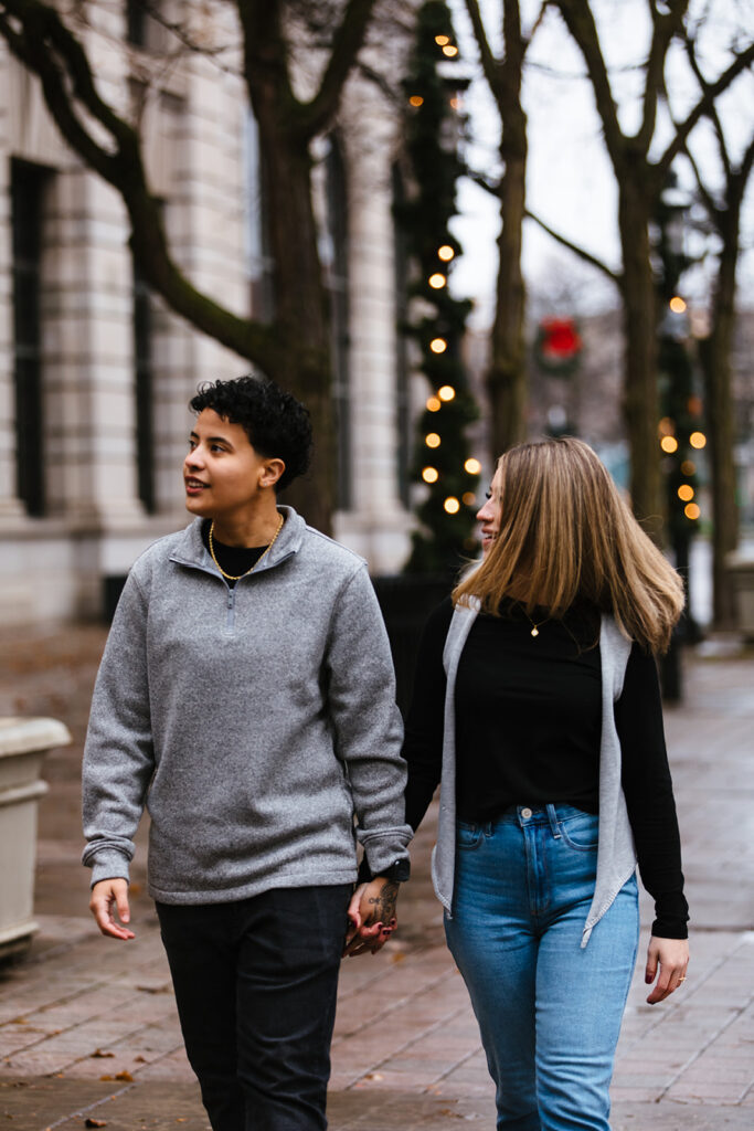 Bride and bride walk holding hands in hanover square in downtown syracuse during their syracuse engagement session.