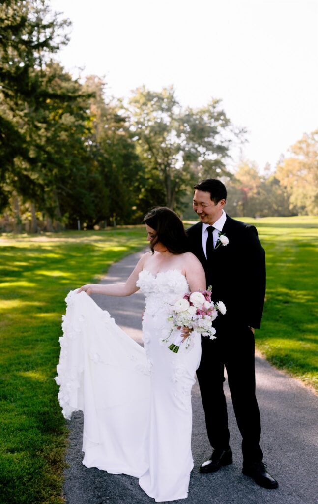 Bride and groom smile as bride holds her dress from Lovely Bride in Victor, NY.