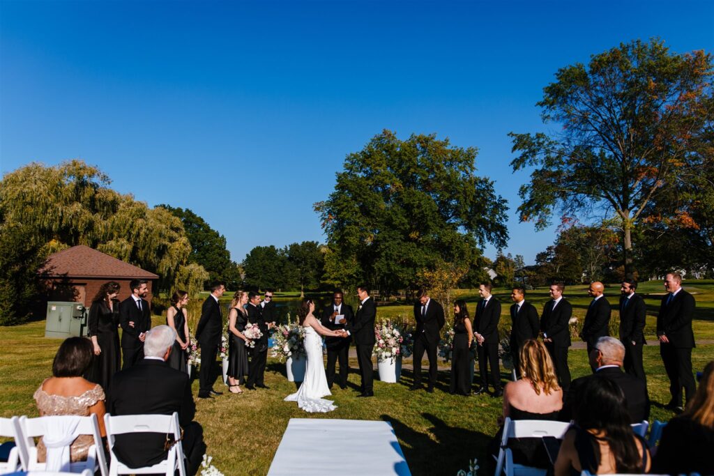 Bride and groom hold hands at their Locust Hill country club wedding ceremony. They were married in late September in Rochester, NY.