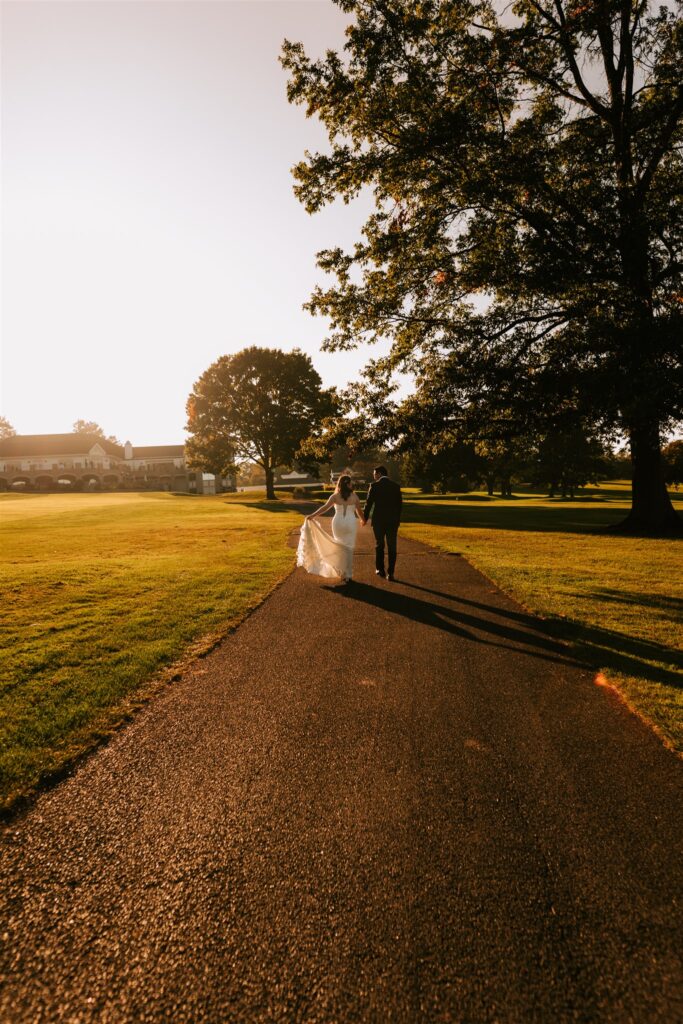 Bride and groom walk towards the Locust Hill Country Club as golden light surrounds them on their wedding day. 