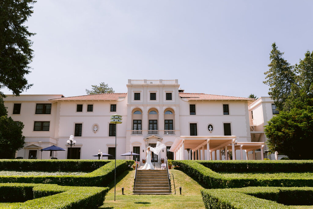 A bride walking down a staircase in front of a mansion towards a garden 
