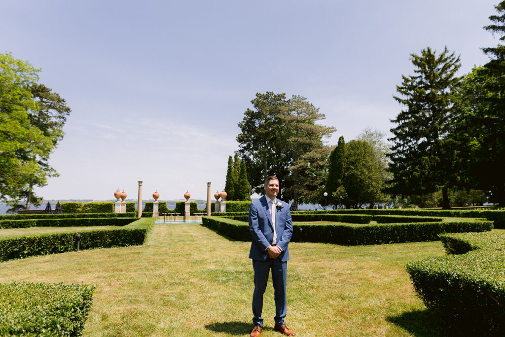 A groom standing in the middle of a garden area smiling 