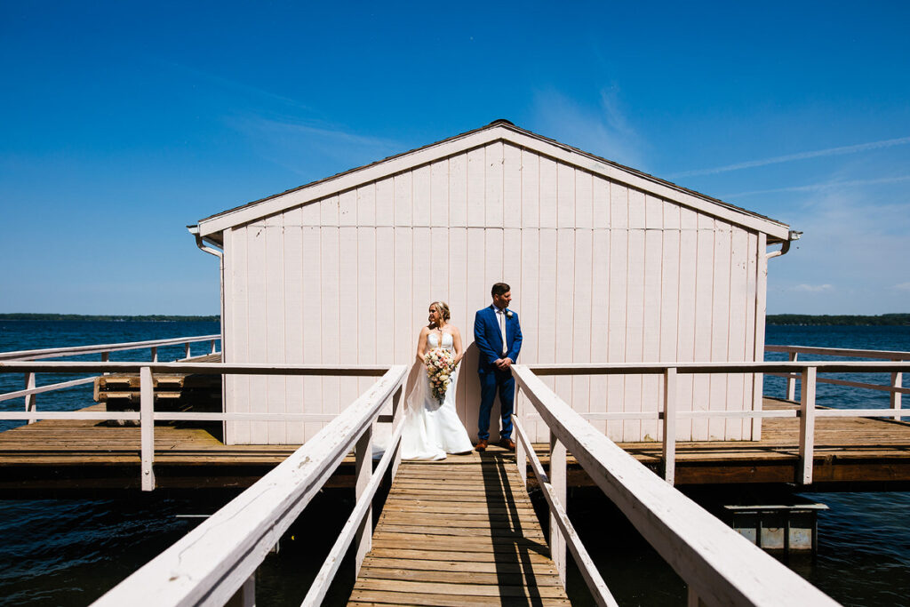 A newlywed couple standing on a dock looking opposite directions 