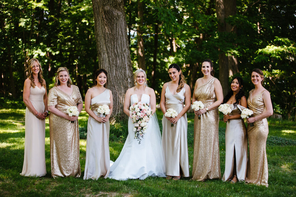 A wedding party in gold dresses smiling in a wooded area 