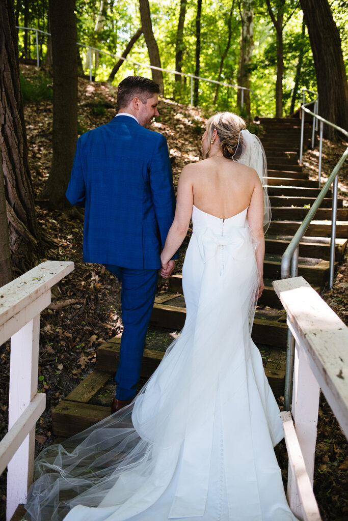 A newlywed couple walking up a wooden staircase in a forest 