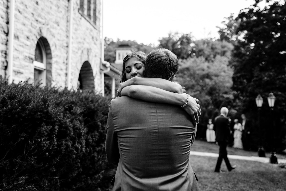 A black-and-white photo of two people hugging outside a stone building showing off documentary style wedding phtoography