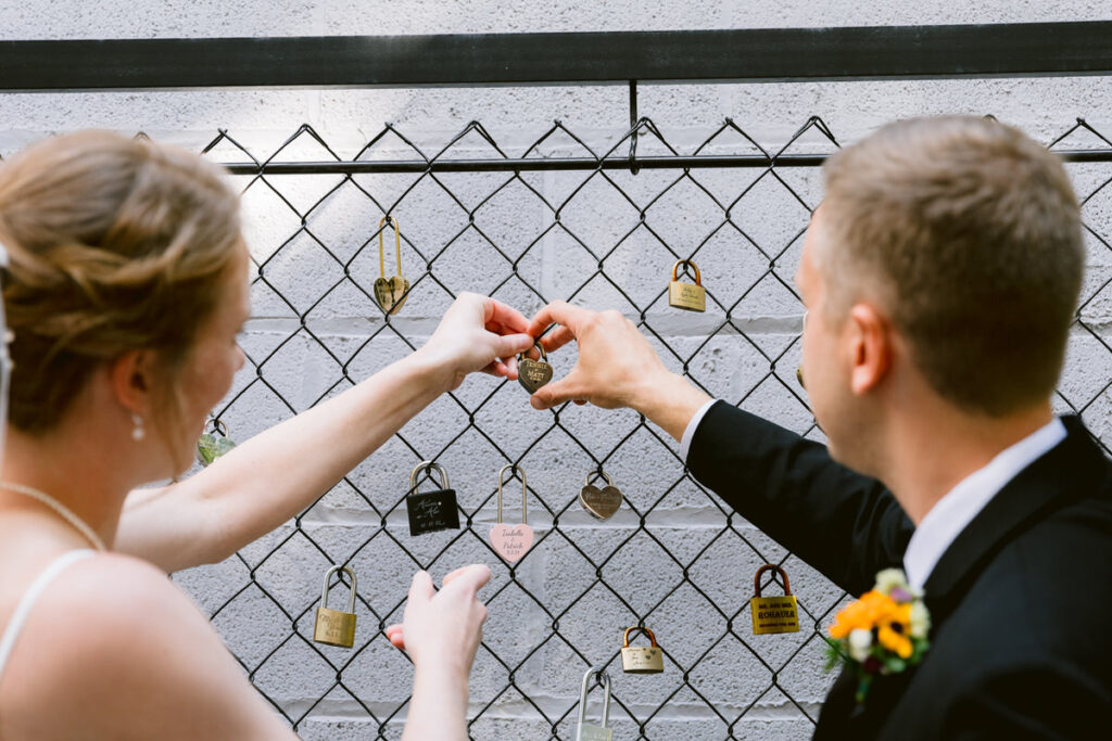 A bride and groom attaching a personalized lock to a fence.