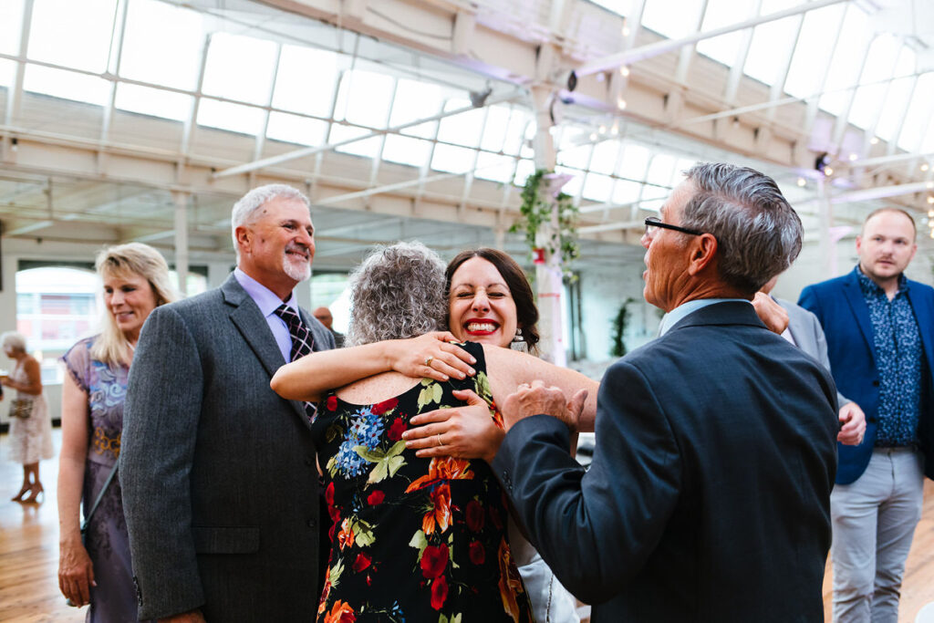 A woman hugging a guest while others stand nearby in a bright venue.