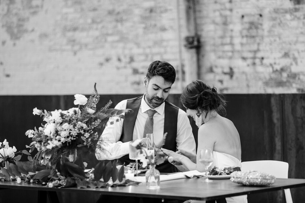 A newlywed couple sitting a reception table looking at their rings 