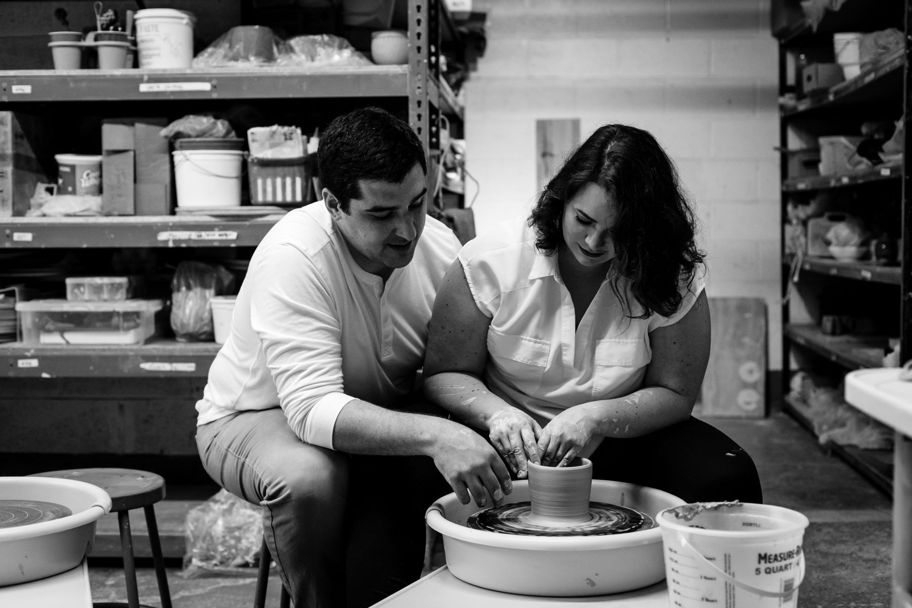 a woman and a man sitting on stools in a pottery studio both are working together to make pottery 