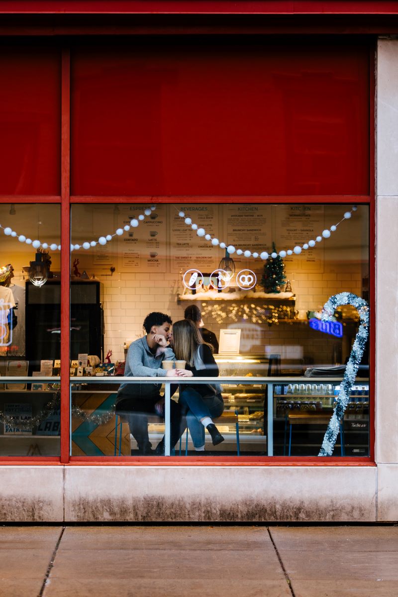 A couple inside of a coffee shop giving each other a kiss with two coffees in front of them 