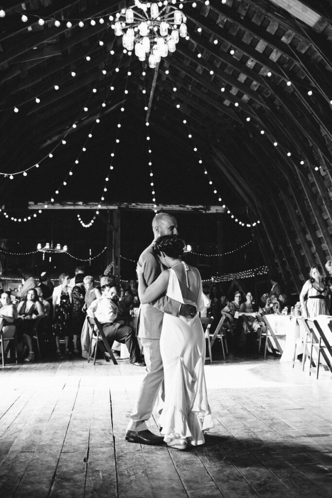 The bride and groom dancing under twinkling string lights in a beautifully lit barn. 