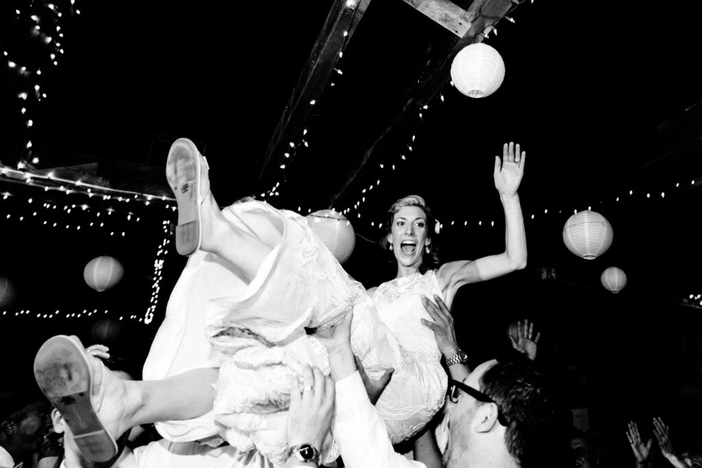 The bride joyfully being lifted into the air by guests during a celebration. 