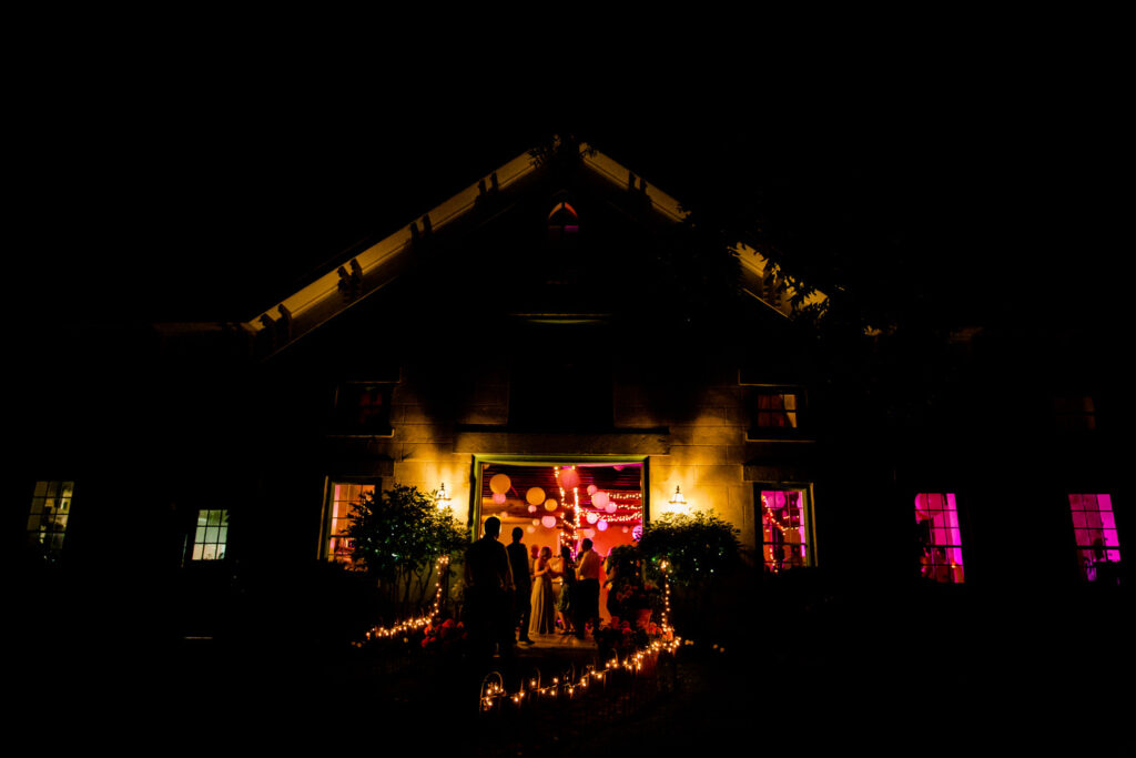 The Frogpond venue glows warmly at night, with lights illuminating the entrance and guests seen inside enjoying the celebration.