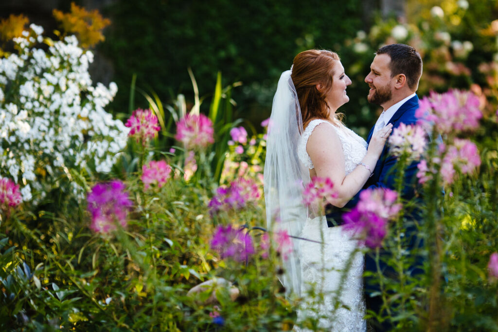 The bride and groom gaze lovingly at each other in a garden of vibrant pink, white, and purple flowers. 