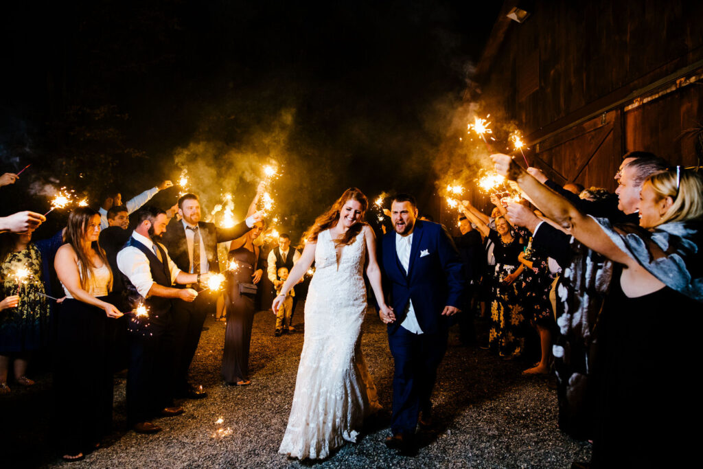 The bride and groom walk through a joyful crowd of guests holding sparklers.